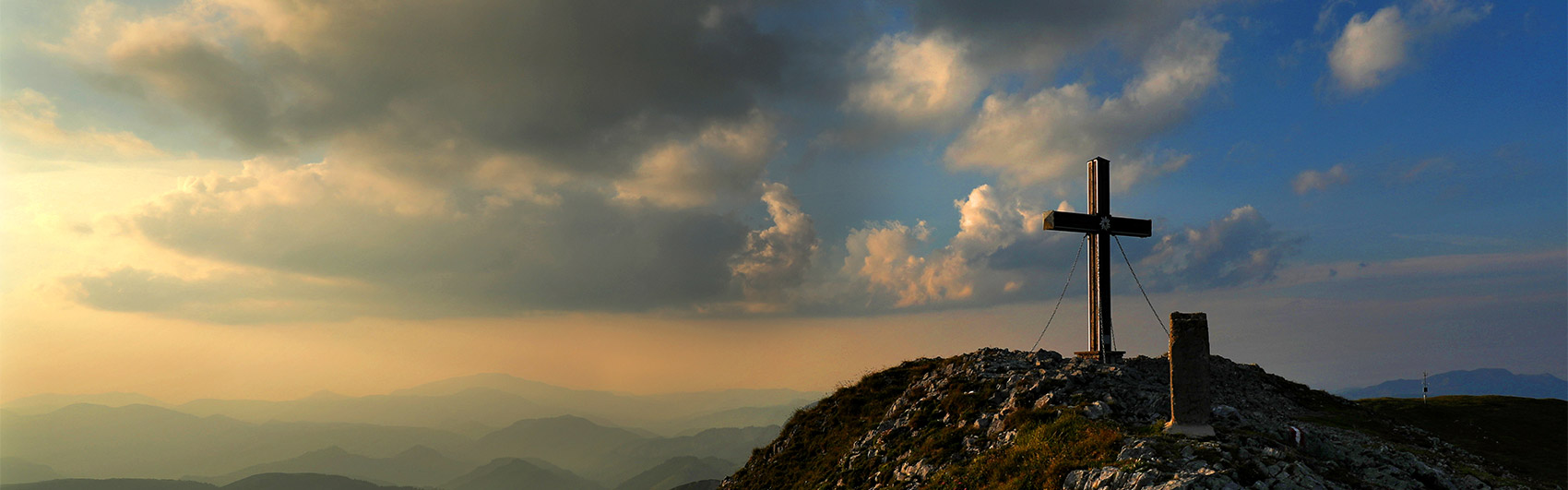 Im rechten Bildbereich - Gipfelkreuz auf einer Bergkuppel bei Sonnenuntergang
