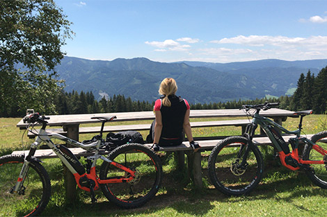 Radfahrerin sitzt auf einer Bank und genießt den Blick auf die Berge